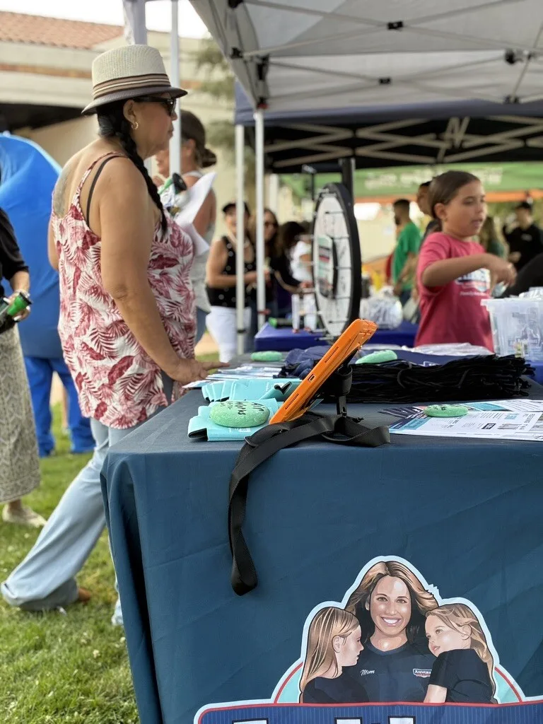 The AirWorks booth table at a community concert, with a prize wheel and neighbours stopping by.