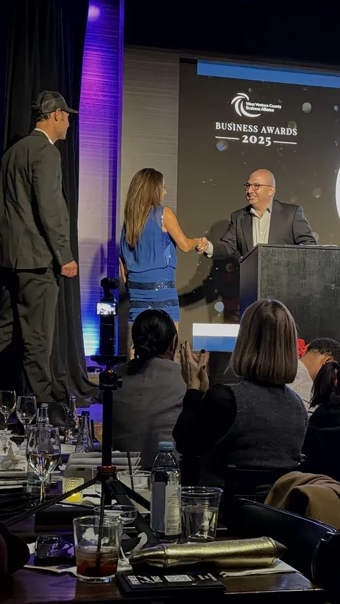 Stephanie Allen shakes hands with the presenter on stage at the WVCBA Business Awards, with the Business Awards 2025 screen behind her.
